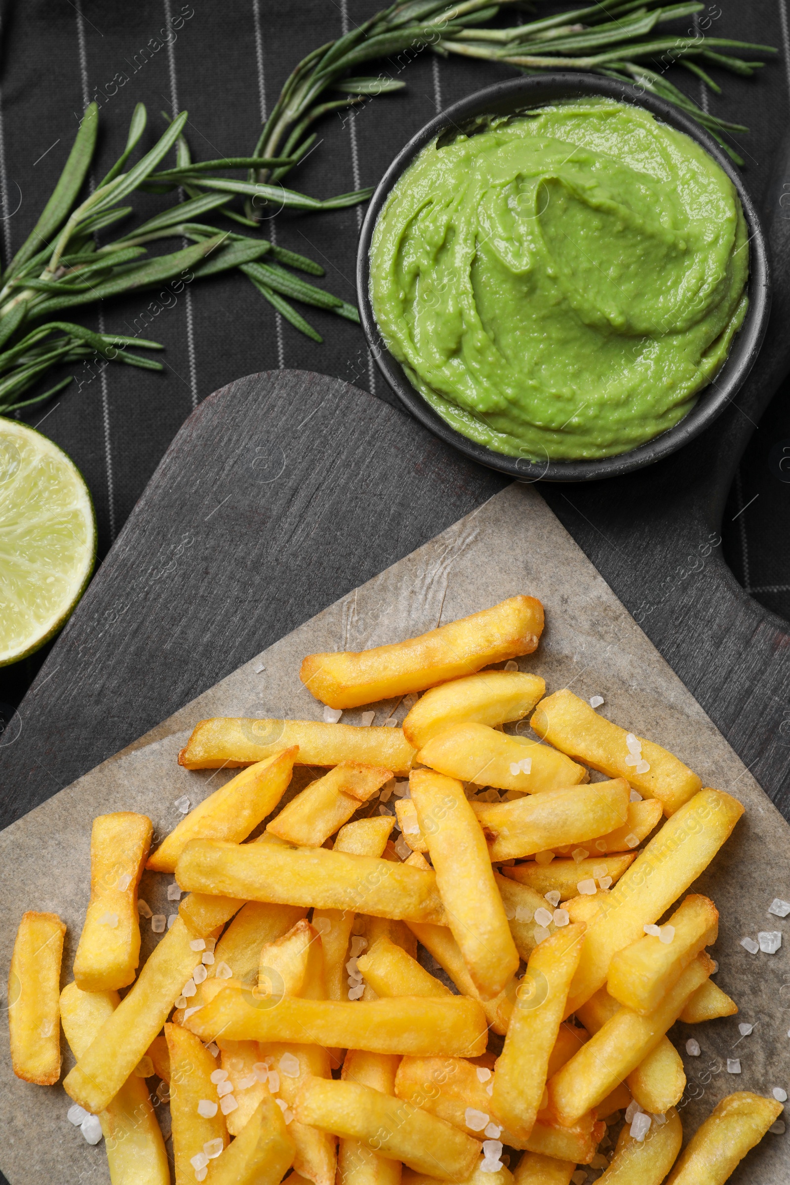 Photo of Serving board with french fries, avocado dip, lime and rosemary on cloth, flat lay