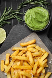 Photo of Serving board with french fries, avocado dip, lime and rosemary on cloth, flat lay