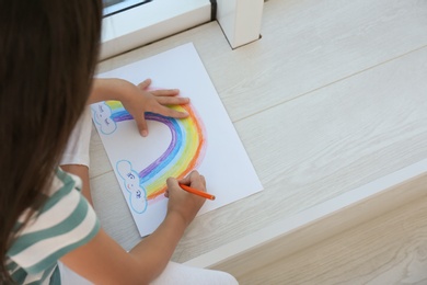 Photo of Little girl drawing rainbow indoors, above view. Stay at home concept