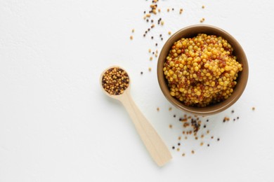 Fresh whole grain mustard in bowl and dry seeds on white table, flat lay. Space for text