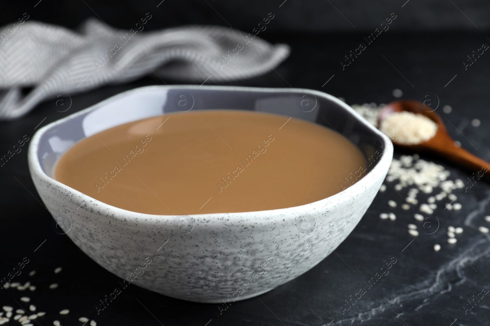 Photo of Tasty sesame paste in bowl on black table, closeup