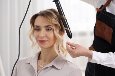 Hair styling. Hairdresser curling woman's hair indoors, closeup