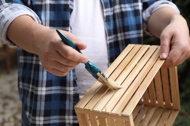 Man applying varnish onto wooden crate against blurred background, closeup