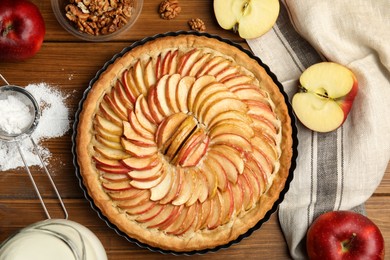 Delicious homemade apple tart and ingredients on wooden table, flat lay