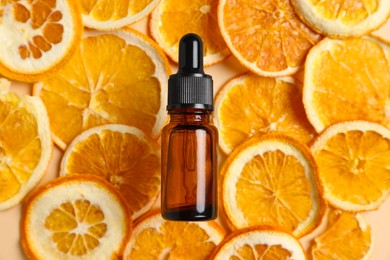 Bottle of organic cosmetic product and dried orange slices on beige background, flat lay