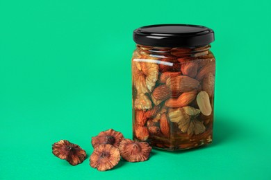 Photo of Jar with different tasty nuts and honey on green background, space for text