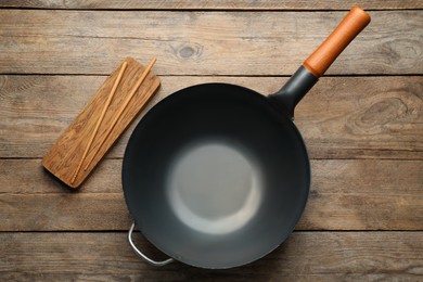 Photo of Empty iron wok with chopsticks on wooden table, flat lay