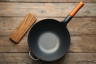 Empty iron wok with chopsticks on wooden table, flat lay