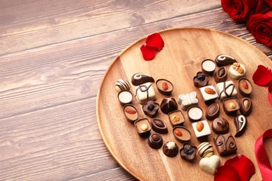 Photo of Heart made with delicious chocolate candies and rose petals on wooden table. Space for text