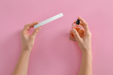 Photo of Woman with bottle of perfume and blotter on pink background, top view