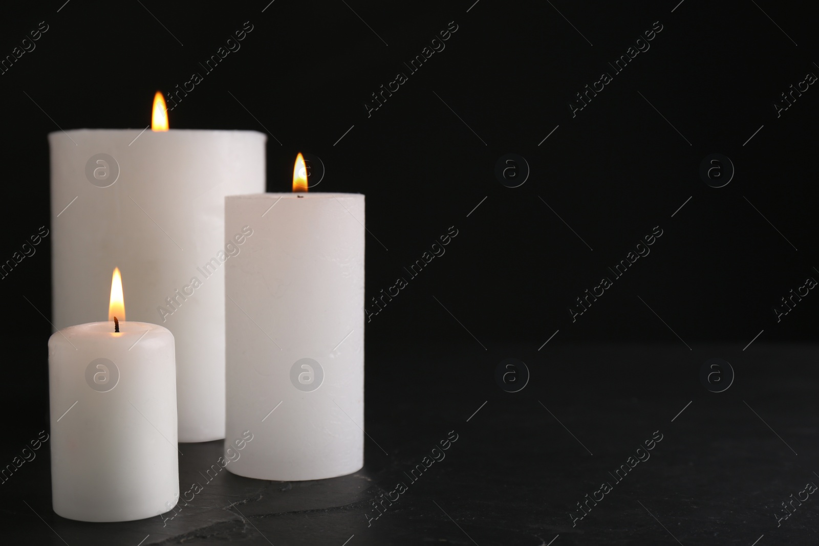 Photo of Burning candles on slate table against black background. Space for text