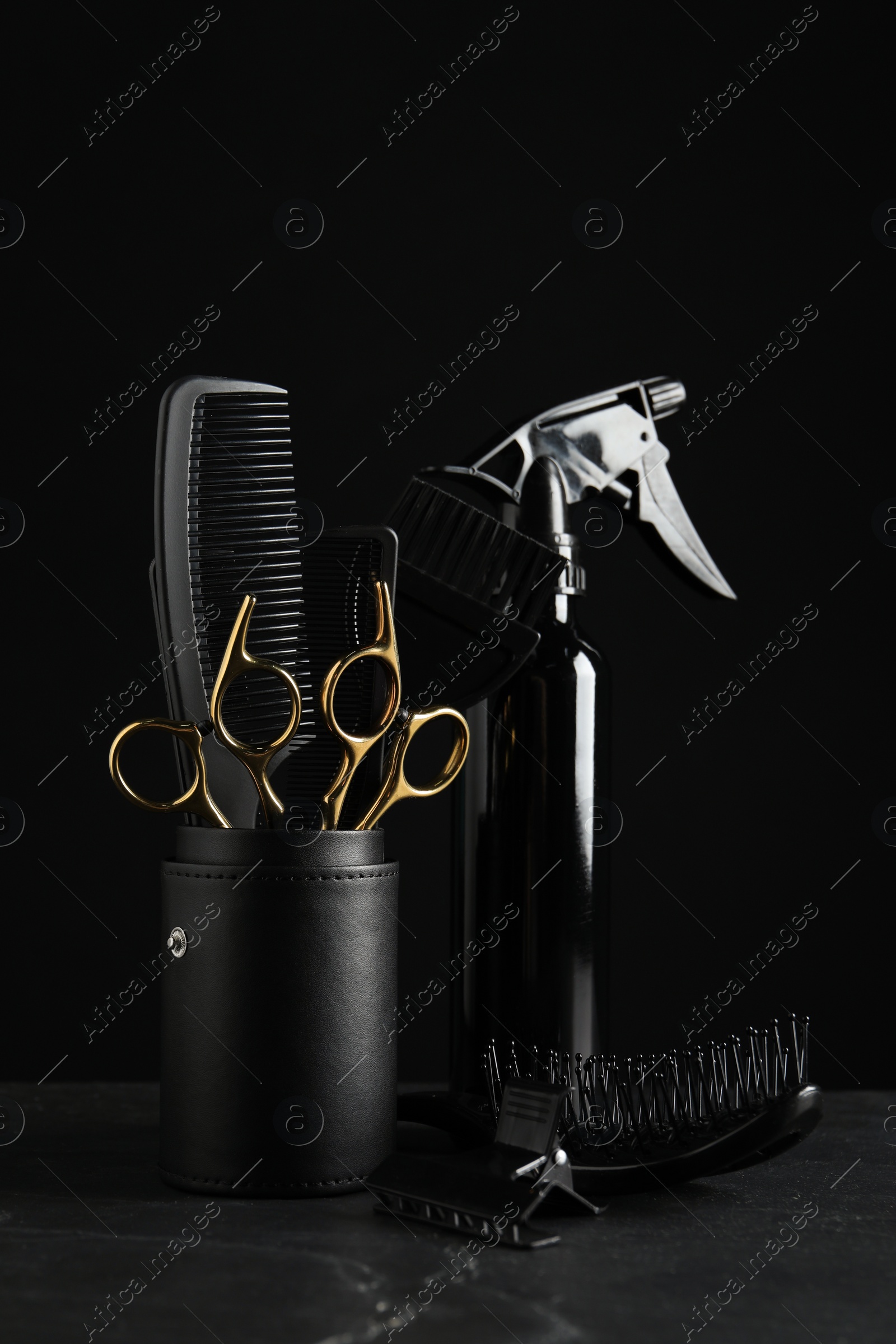 Photo of Different hairdresser tools on grey table against black background