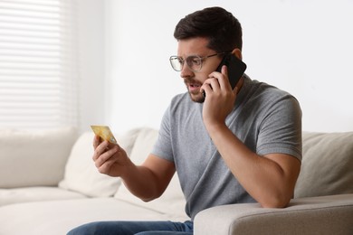 Upset man with credit card talking on smartphone at home. Be careful - fraud