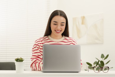 Photo of Woman using laptop at white table indoors