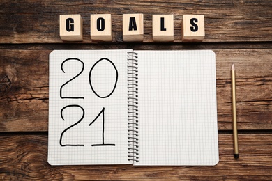 Word Goals made of cubes near notebook with number 2021, new year goals. Objects on wooden table, flat lay
