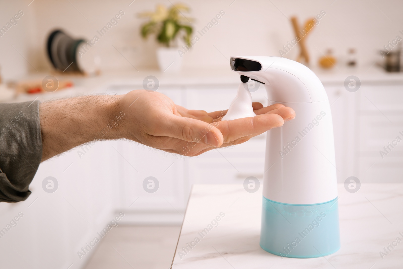 Photo of Man using automatic soap dispenser in kitchen, closeup