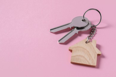 Photo of Metallic keys with wooden keychain in shape of house on pink background, space for text