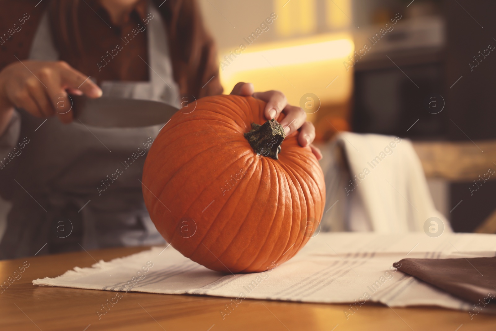 Photo of Woman carving pumpkin at table in kitchen. Halloween celebration