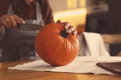Photo of Woman carving pumpkin at table in kitchen. Halloween celebration