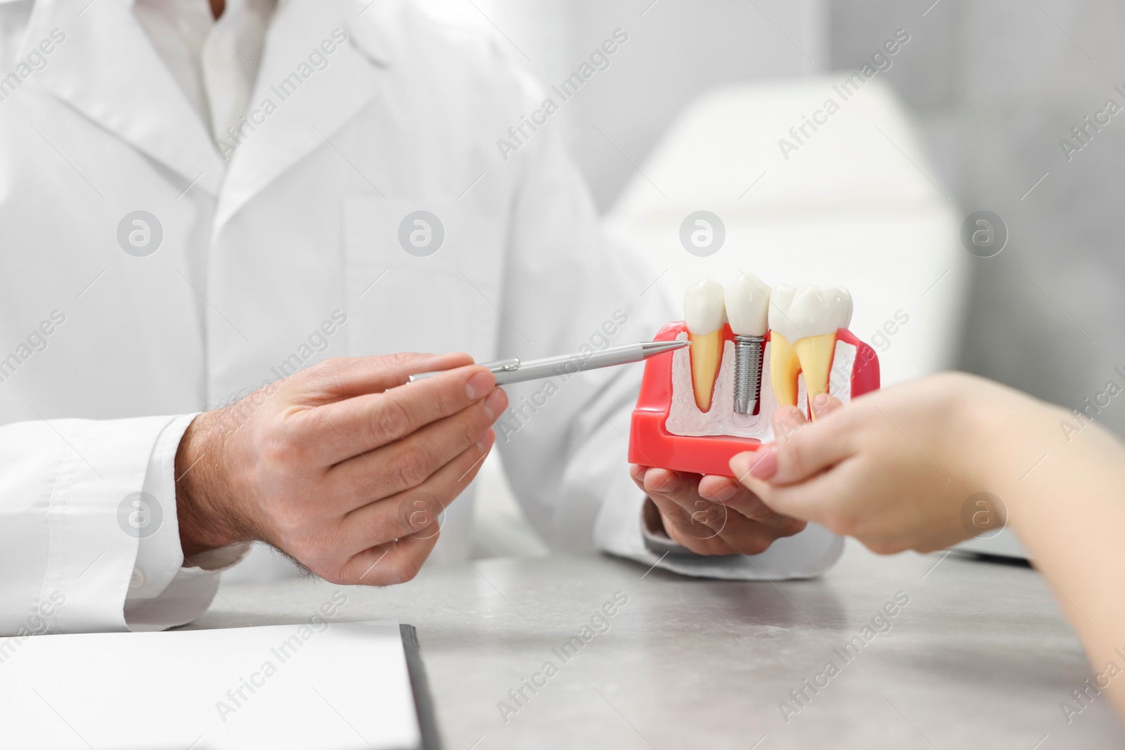 Photo of Doctor showing patient educational model of dental implant in clinic, closeup