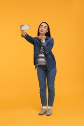 Photo of Young woman taking selfie with smartphone and blowing kiss on yellow background