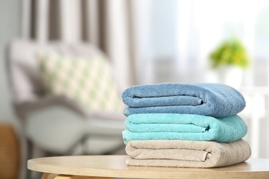 Photo of Stack of folded clean soft towels on table indoors. Space for text