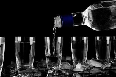 Photo of Pouring vodka into shot glass on black background