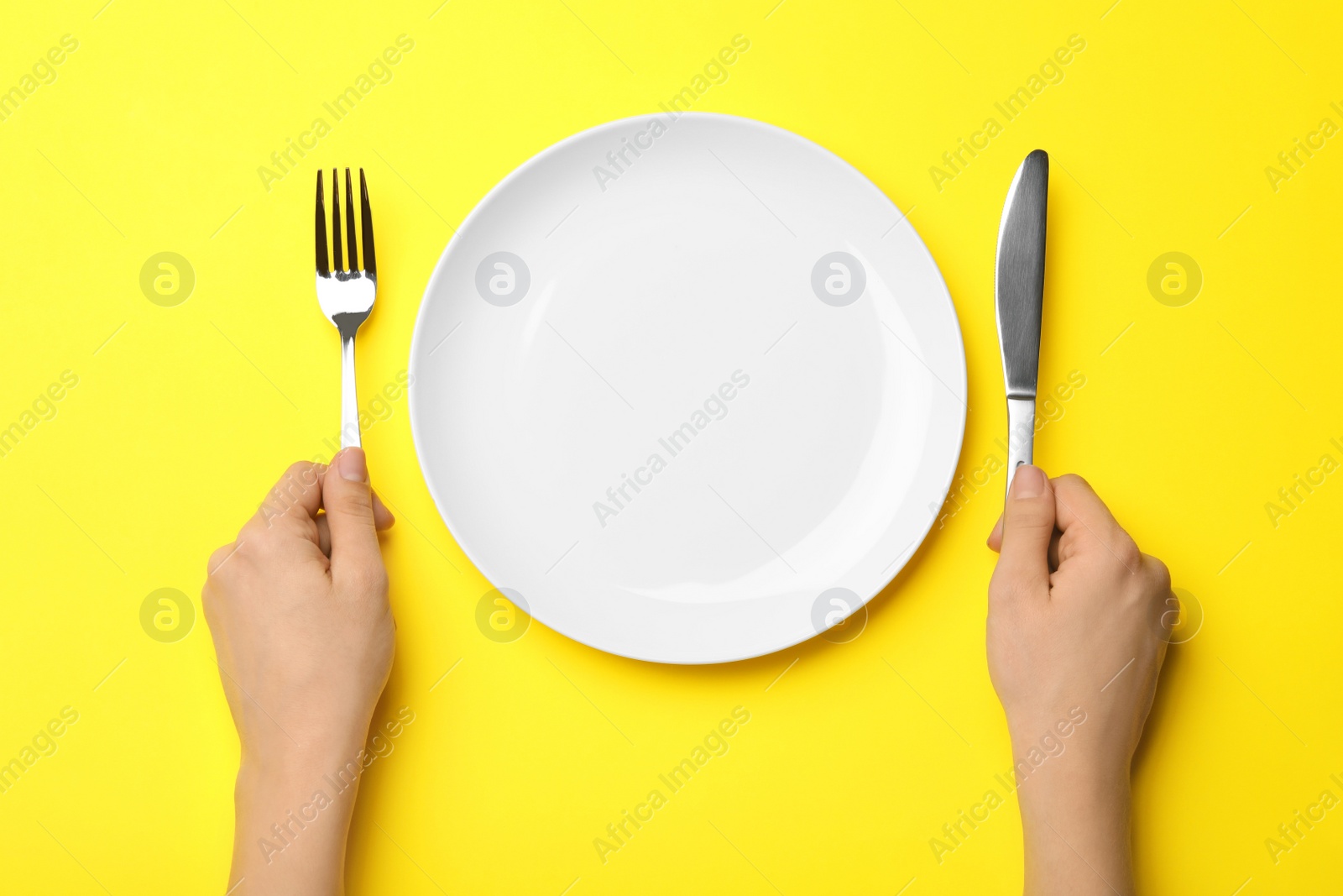 Photo of Woman with fork, knife and empty plate on color background, top view