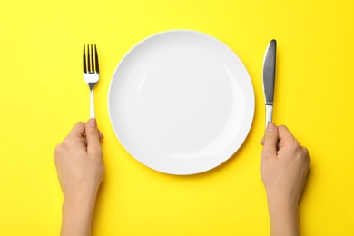 Woman with fork, knife and empty plate on color background, top view