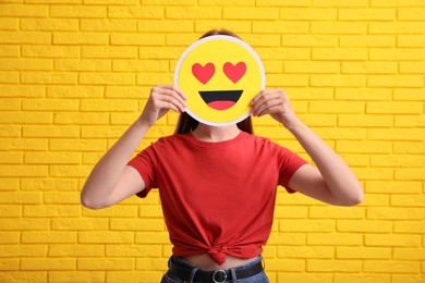 Woman covering face with heart eyes emoji near yellow brick wall