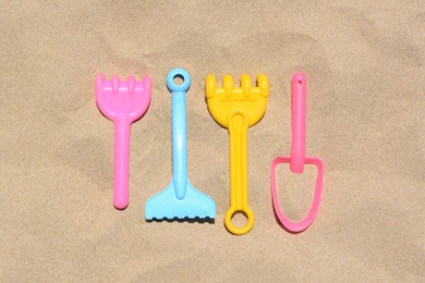 Bright plastic rakes and shovel on sand, flat lay. Beach toys