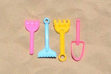 Photo of Bright plastic rakes and shovel on sand, flat lay. Beach toys