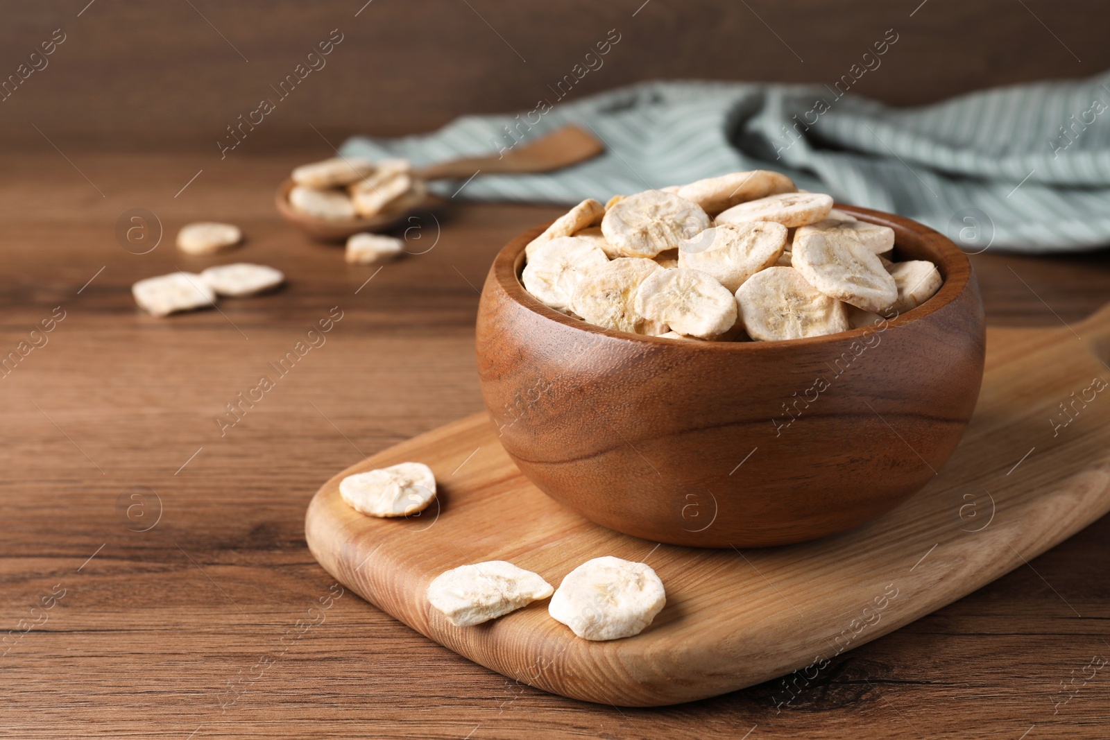 Photo of Bowl and dried banana slices on wooden table. Space for text