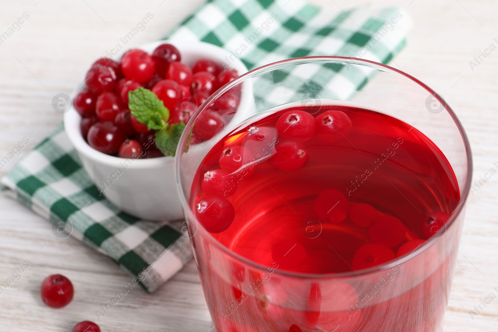 Photo of Tasty cranberry juice in glass and fresh berries on white wooden table, closeup