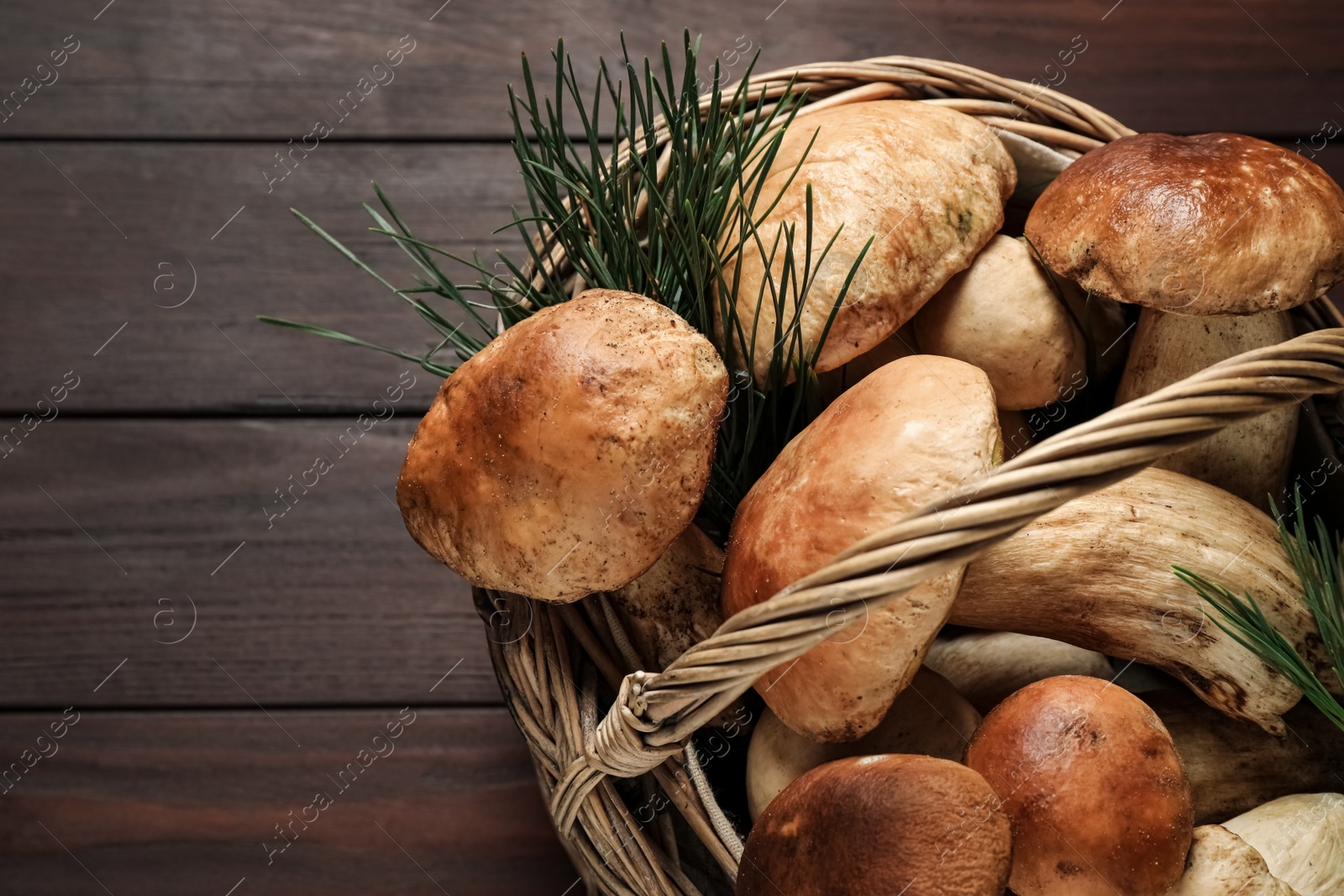 Photo of Fresh wild mushrooms in wicker basket on wooden table, closeup