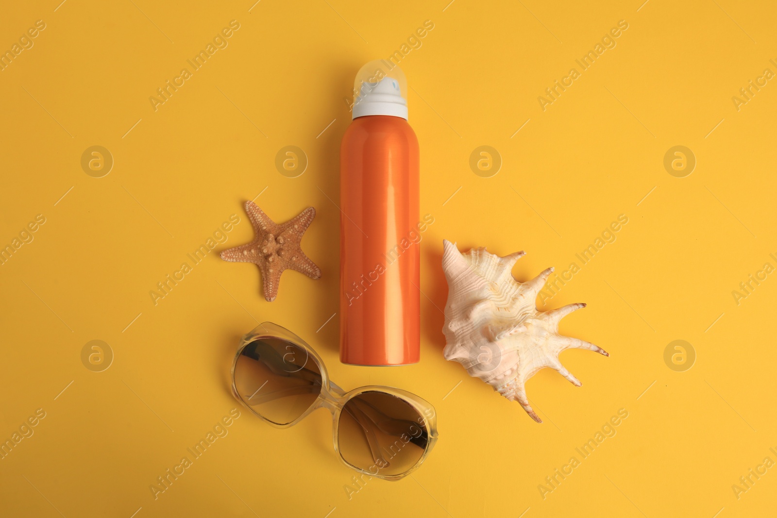 Photo of Bottle of sunscreen, starfish, seashell and sunglasses on yellow background, flat lay