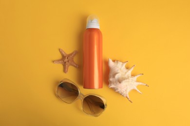 Bottle of sunscreen, starfish, seashell and sunglasses on yellow background, flat lay