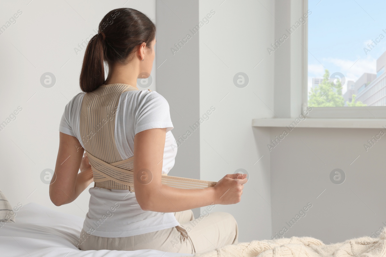 Photo of Woman with orthopedic corset sitting in bedroom, back view