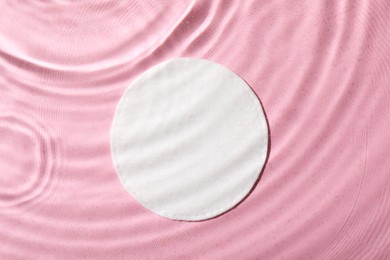 Photo of White cotton pad in water on pink background, top view