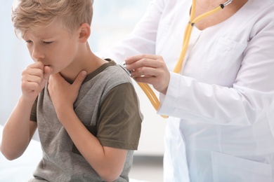 Doctor examining coughing little boy at clinic