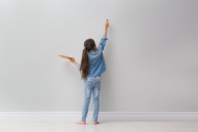 Photo of Little girl painting on light grey wall indoors, back view. Space for text