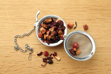 Photo of Snap infuser with dried herbal tea leaves and fruits on wooden table, flat lay