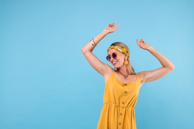 Photo of Portrait of smiling hippie woman in sunglasses dancing on light blue background. Space for text