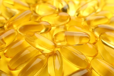 Many vitamin capsules on yellow background, closeup