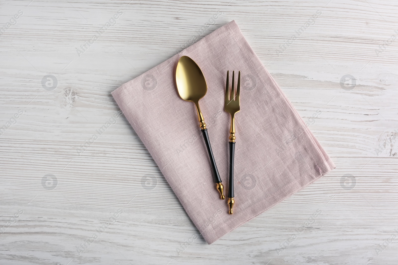 Photo of Shiny fork, spoon and napkin on white wooden table, top view