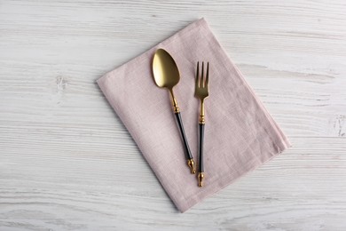 Photo of Shiny fork, spoon and napkin on white wooden table, top view