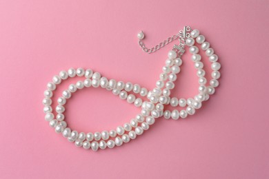 Elegant necklace with pearls on pink background, top view