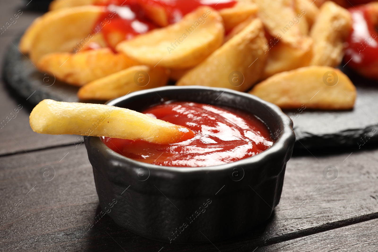 Photo of Delicious french fry with tasty ketchup on dark wooden table, closeup