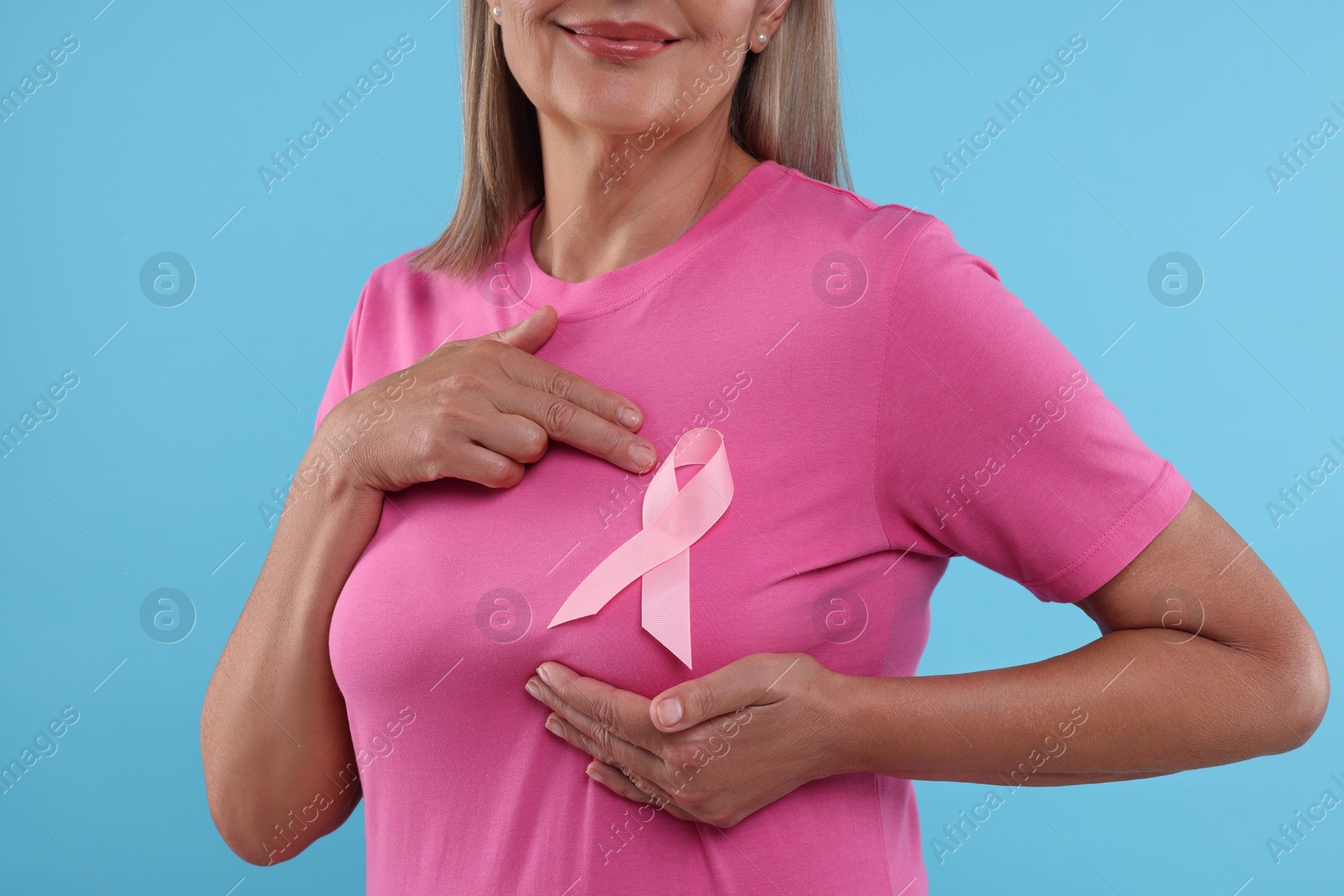 Photo of Woman with pink ribbon on light blue background, closeup. Breast cancer awareness