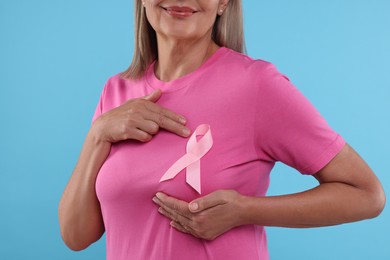 Woman with pink ribbon on light blue background, closeup. Breast cancer awareness